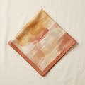 Chiara watercolour square scarf in ochre and terracotta, folded on a cream studio backdrop