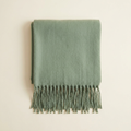 Livia fringed blanket scarf in muted sage with long tassels, folded on a cream studio backdrop